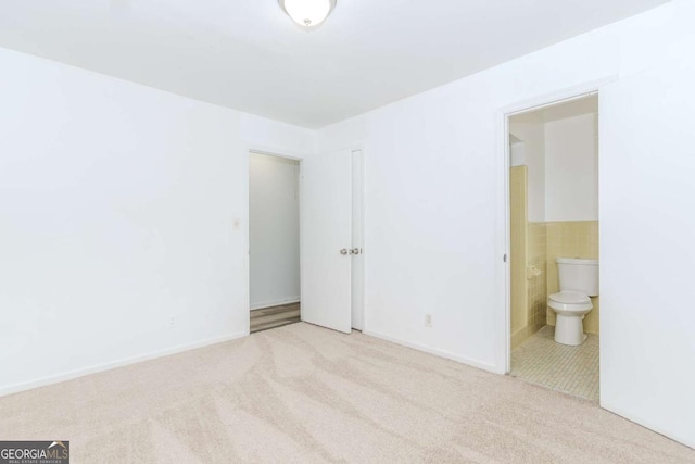 unfurnished bedroom featuring tile walls, connected bathroom, and light colored carpet