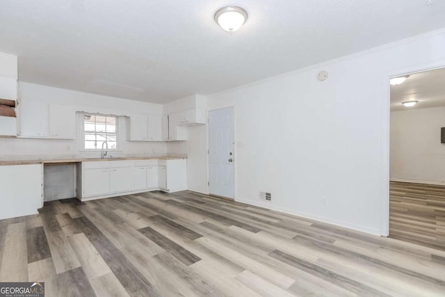 kitchen with white cabinetry, sink, light hardwood / wood-style flooring, and ornamental molding