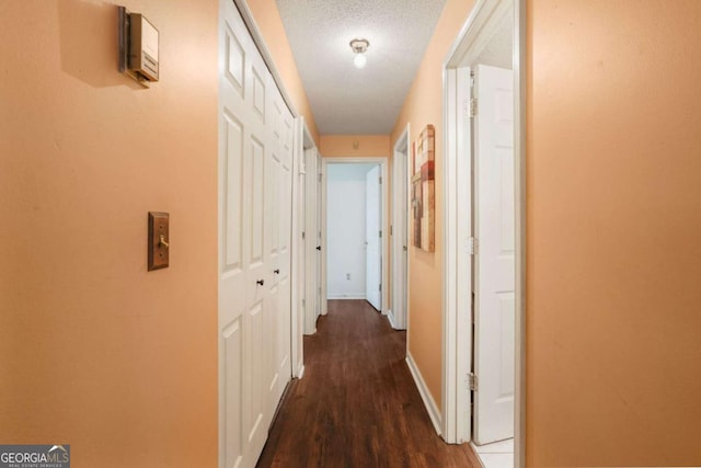 corridor with a textured ceiling and dark hardwood / wood-style flooring