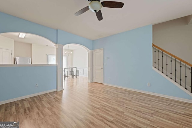 unfurnished living room featuring ceiling fan with notable chandelier and light wood-type flooring