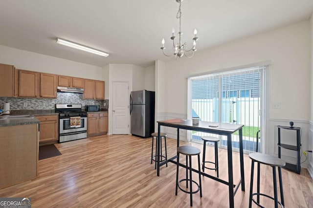 kitchen with an inviting chandelier, hanging light fixtures, light wood-type flooring, stainless steel appliances, and backsplash