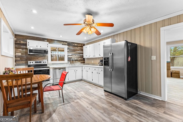 kitchen with light wood finished floors, appliances with stainless steel finishes, ornamental molding, light countertops, and a sink