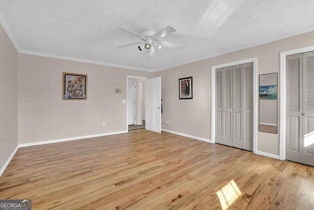 unfurnished bedroom with multiple closets, crown molding, a textured ceiling, and light hardwood / wood-style flooring