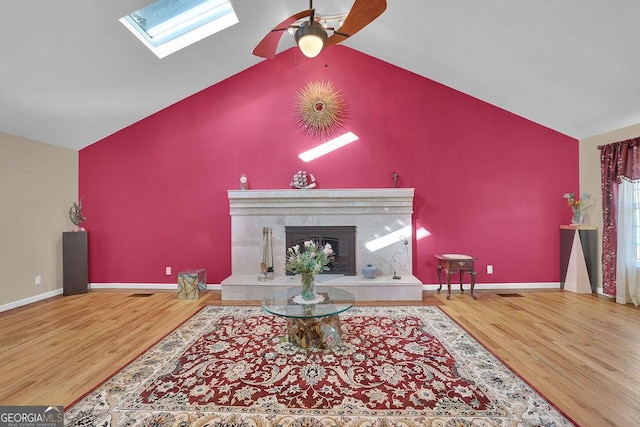 living room with high vaulted ceiling, a skylight, a tiled fireplace, hardwood / wood-style flooring, and ceiling fan