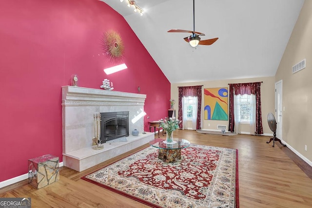 living room featuring ceiling fan, high vaulted ceiling, a high end fireplace, and hardwood / wood-style floors