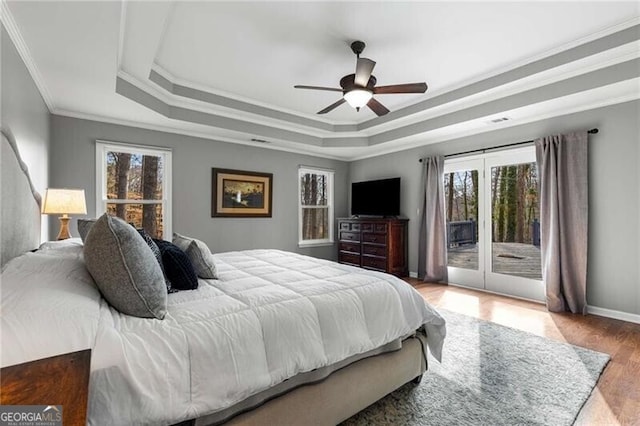 bedroom with multiple windows, access to outside, a raised ceiling, and wood-type flooring