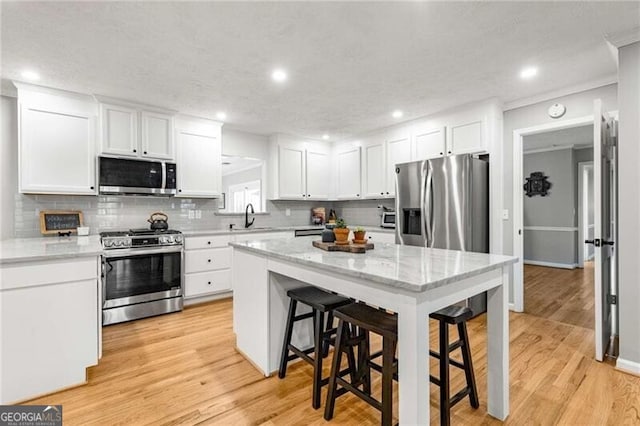 kitchen featuring appliances with stainless steel finishes, sink, white cabinets, a kitchen bar, and light stone counters