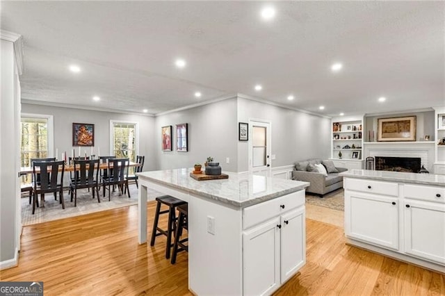 kitchen with white cabinetry, a center island, light stone countertops, and light wood-type flooring