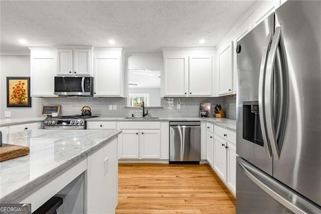 kitchen with sink, stainless steel appliances, light stone counters, white cabinets, and light wood-type flooring