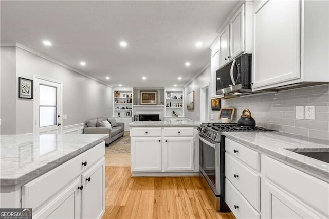 kitchen featuring white cabinetry, stainless steel range with gas stovetop, light stone counters, and light wood-type flooring