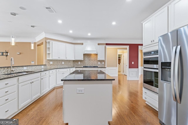 kitchen with premium range hood, sink, decorative light fixtures, appliances with stainless steel finishes, and a kitchen island