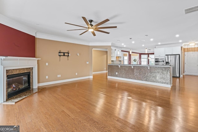 unfurnished living room featuring crown molding, ceiling fan, a high end fireplace, and light wood-type flooring