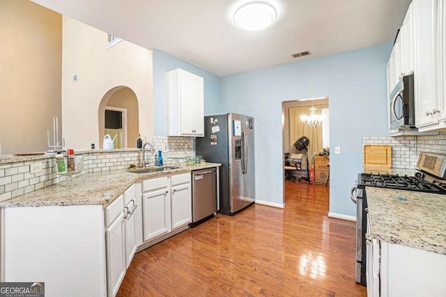 kitchen with stainless steel appliances, white cabinetry, light stone countertops, and sink