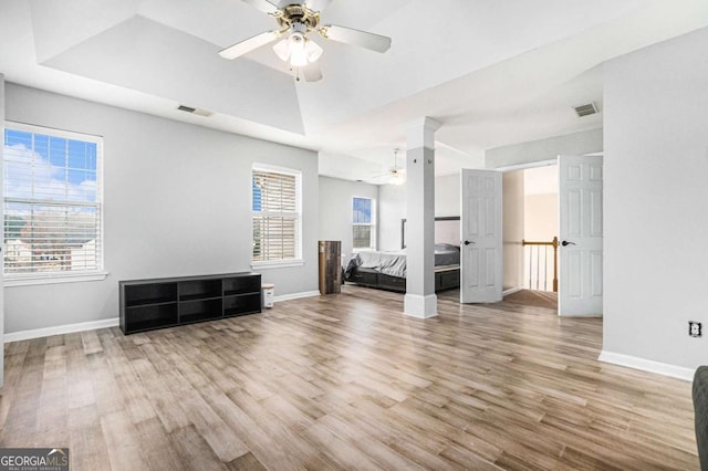 unfurnished bedroom with decorative columns, ceiling fan, light hardwood / wood-style floors, and a tray ceiling