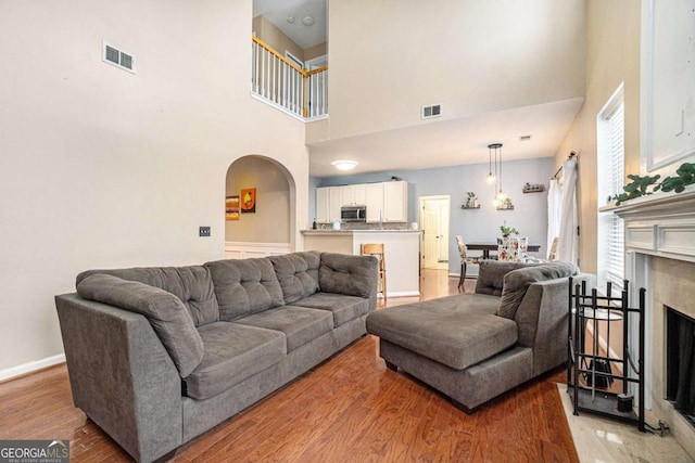 living room with a high end fireplace, wood-type flooring, and a high ceiling