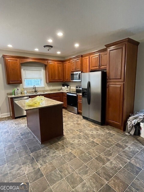 kitchen featuring stainless steel appliances, light stone countertops, a kitchen island, and sink