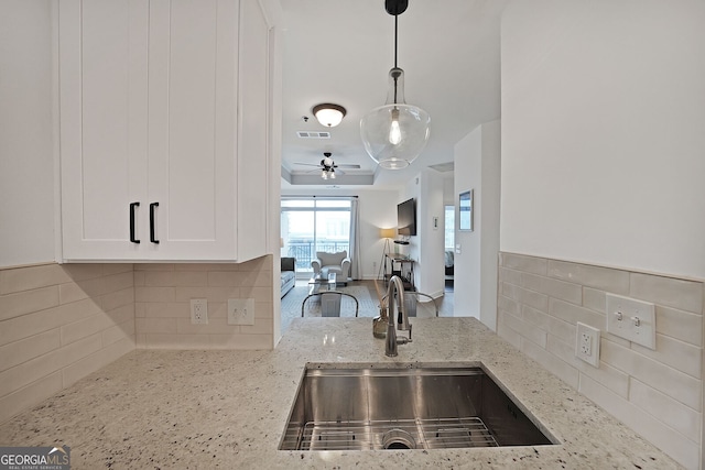 kitchen with sink, white cabinetry, light stone counters, decorative light fixtures, and a raised ceiling