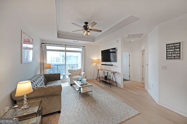 living room featuring a raised ceiling, crown molding, ceiling fan, and light hardwood / wood-style floors