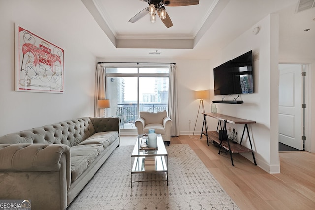 living room with crown molding, a raised ceiling, ceiling fan, and light wood-type flooring