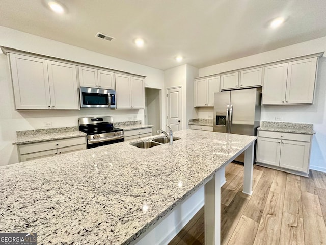 kitchen with sink, a breakfast bar, stainless steel appliances, light hardwood / wood-style floors, and light stone countertops