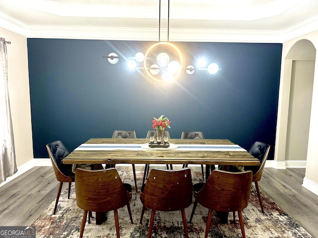 dining space featuring arched walkways, baseboards, wood finished floors, and crown molding