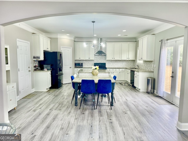 kitchen with decorative backsplash, wall chimney exhaust hood, a kitchen island, light wood-type flooring, and black appliances