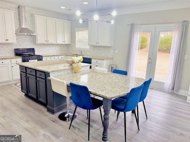 kitchen with wall chimney exhaust hood, white cabinetry, black gas range oven, pendant lighting, and a large island