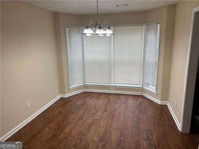 unfurnished dining area featuring dark hardwood / wood-style floors, a notable chandelier, and a textured ceiling