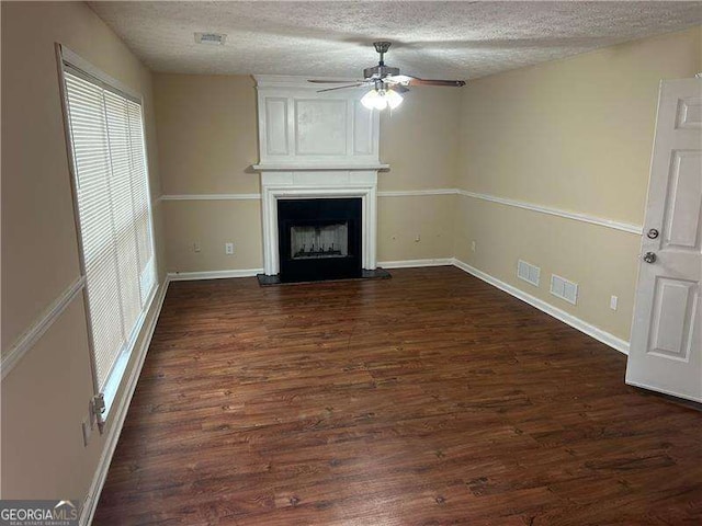 unfurnished living room with ceiling fan, a large fireplace, dark hardwood / wood-style flooring, and a textured ceiling