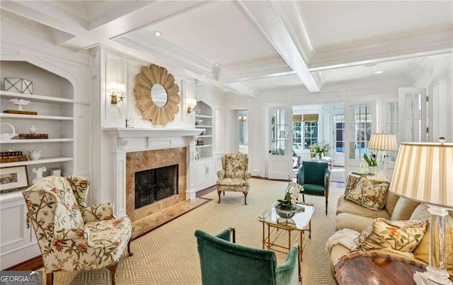 living room featuring beamed ceiling, coffered ceiling, a high end fireplace, crown molding, and built in shelves