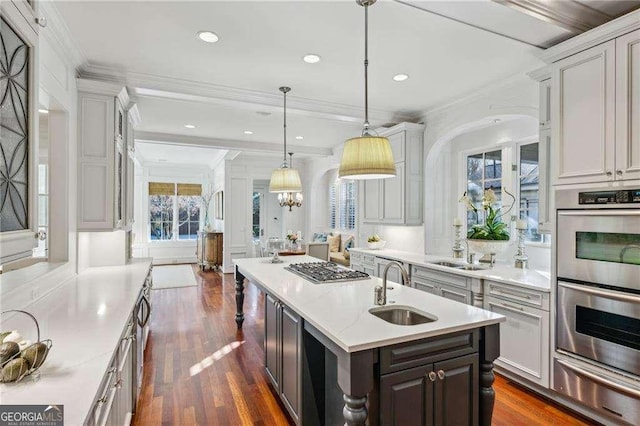 kitchen featuring sink, appliances with stainless steel finishes, hanging light fixtures, ornamental molding, and a center island with sink