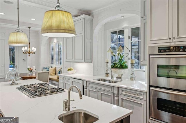 kitchen with sink, decorative light fixtures, ornamental molding, an island with sink, and stainless steel appliances