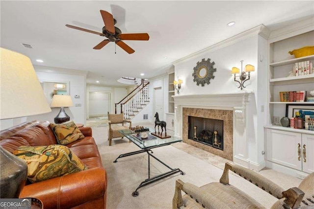 living room featuring crown molding, a premium fireplace, ceiling fan, light carpet, and built in shelves