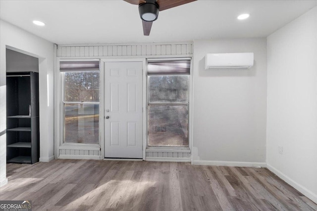 interior space with light hardwood / wood-style flooring, a wall unit AC, and ceiling fan