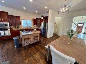 kitchen with a breakfast bar area, an inviting chandelier, a center island, appliances with stainless steel finishes, and dark hardwood / wood-style flooring