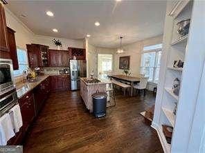 kitchen with dark wood-type flooring, hanging light fixtures, stainless steel refrigerator with ice dispenser, wall oven, and a kitchen island