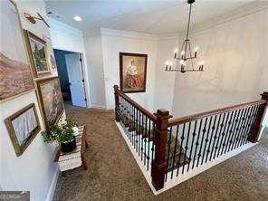 hallway with an inviting chandelier, ornamental molding, and dark colored carpet