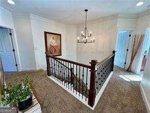 hall with crown molding, carpet flooring, and a chandelier