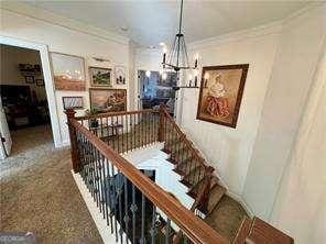 staircase with an inviting chandelier, ornamental molding, and carpet floors