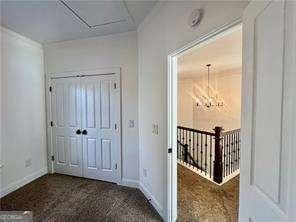 hallway with a notable chandelier and dark colored carpet