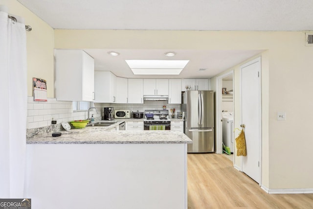 kitchen with sink, range with gas cooktop, stainless steel fridge, kitchen peninsula, and white cabinets