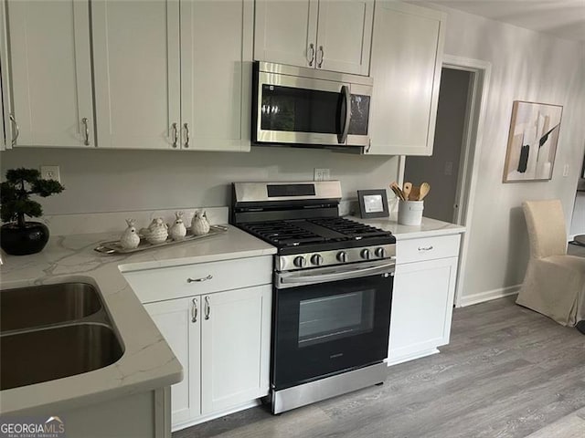 kitchen featuring sink, appliances with stainless steel finishes, white cabinetry, light stone counters, and light hardwood / wood-style floors