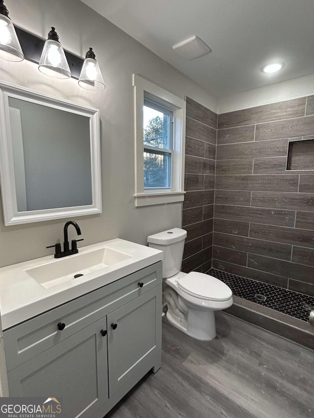 bathroom with vanity, wood-type flooring, a tile shower, and toilet