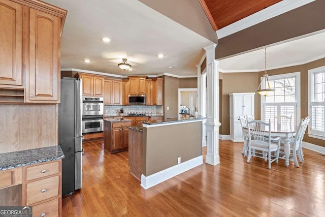 kitchen with dark stone countertops, decorative columns, appliances with stainless steel finishes, and a kitchen island