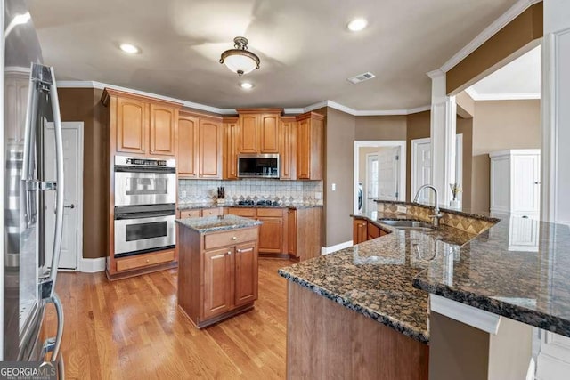 kitchen featuring sink, dark stone counters, a kitchen island with sink, light hardwood / wood-style floors, and stainless steel appliances