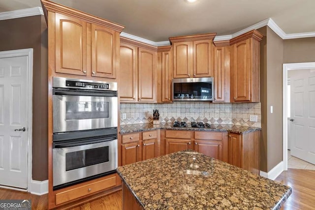 kitchen featuring tasteful backsplash, ornamental molding, stainless steel appliances, and dark stone counters