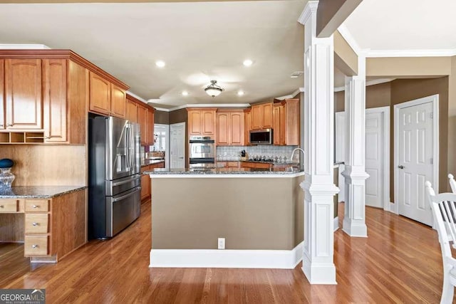 kitchen with stainless steel appliances, hardwood / wood-style flooring, decorative columns, and dark stone counters