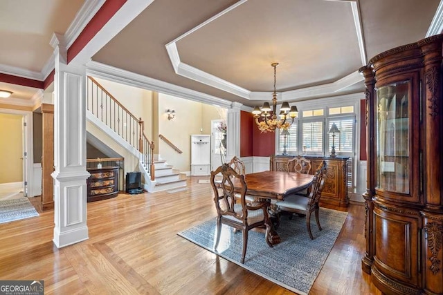 dining area with hardwood / wood-style flooring, a notable chandelier, a tray ceiling, ornamental molding, and ornate columns