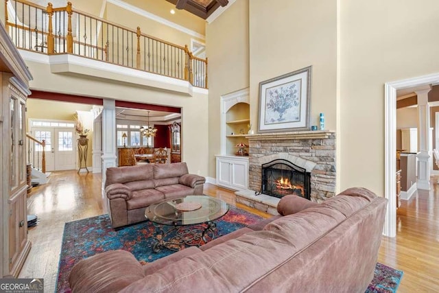 living room featuring crown molding, light hardwood / wood-style flooring, decorative columns, built in shelves, and a stone fireplace