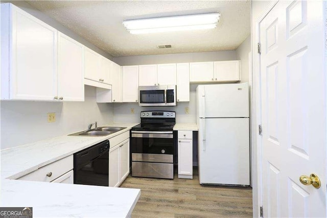 kitchen with stainless steel appliances, sink, white cabinets, and light hardwood / wood-style floors